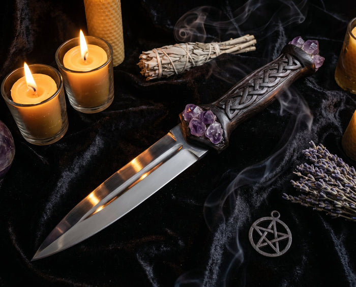 Black-hilted ritual blade with amethyst and carved knotwork on dark velvet beside lit candles