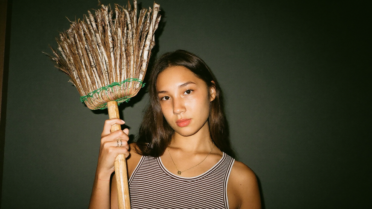 Young woman holding a hand-bound birch twig besom against a dark green wall