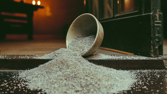 Coarse sea salt spilling from a tipped ceramic bowl across a dark wooden doorway threshold