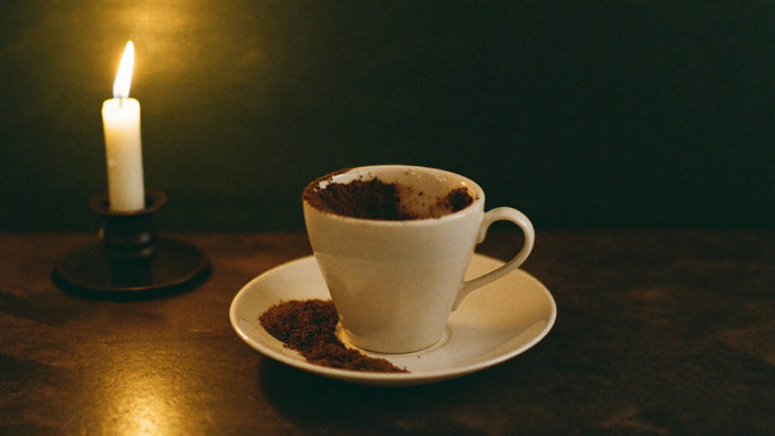 A white cup and saucer with scattered coffee grounds on a dark table and steam rising from the cup
