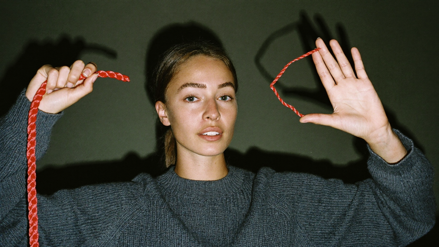 Woman holding both ends of a red cord she has just cut, hands raised against a dark wall