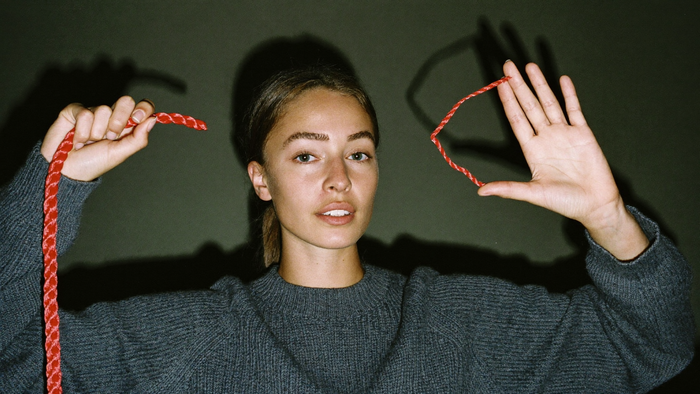 Woman holding both ends of a red cord she has just cut, hands raised against a dark wall