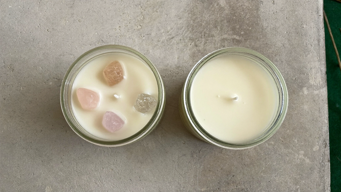 Two unlit candles seen from directly above on pale concrete, the left one set with rose quartz stones in the wax