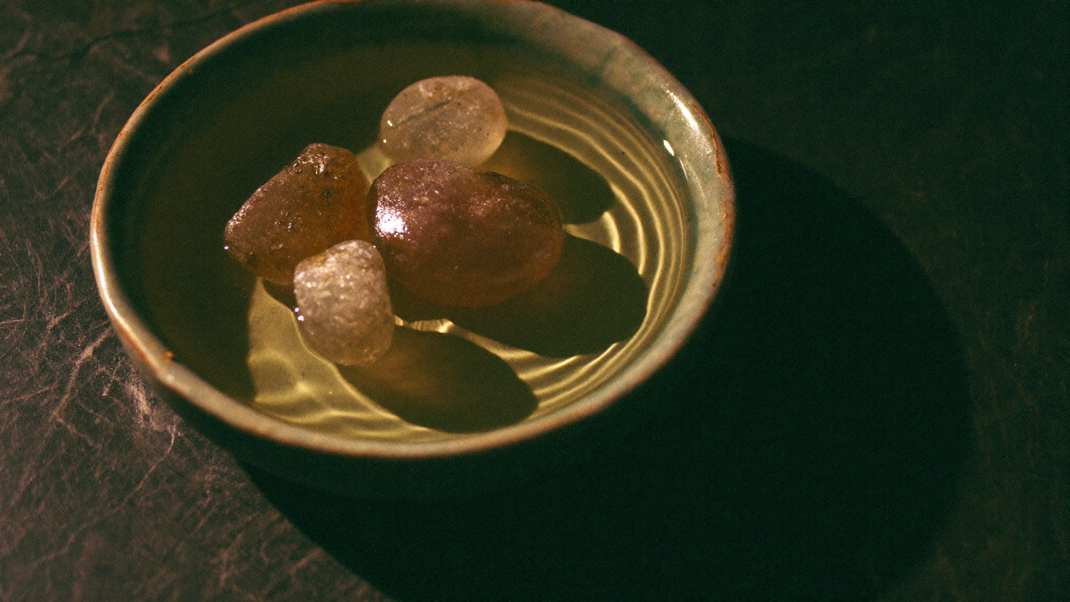 Tumbled quartz stones lying in a shallow ceramic dish of clear water on a dark stone surface