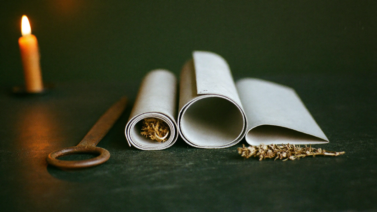 Three rolled blank lead sheets beside a rusted iron nail, a candle and dried herbs