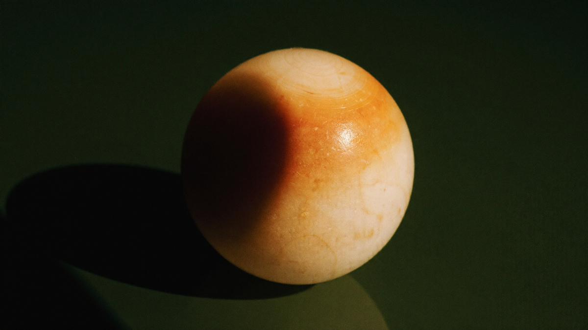 Pale stone sphere on a dark green surface with a curved shadow falling across one side of it