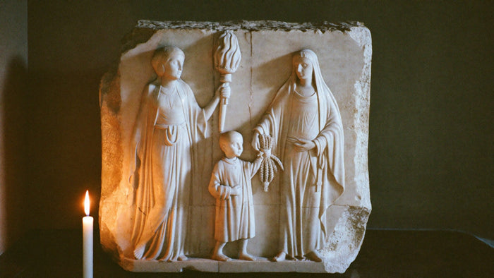 Marble relief by candlelight: a goddess with a torch and another handing ears of grain to a boy, Demeter and Persephone