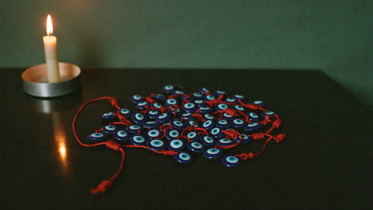 Blue nazar eye beads on red cords spread on a dark altar table beside a burning candle