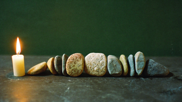 Nine polished stones arranged in a row on dark slate beside a lit candle