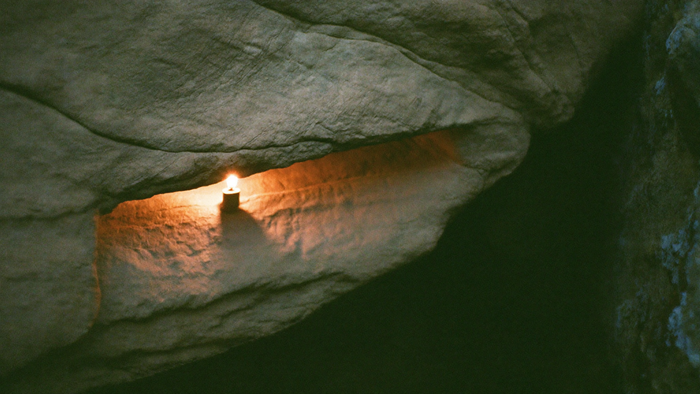 Warm candlelight falling through a narrow pale sandstone cleft, echoing the sun hole of the Externsteine