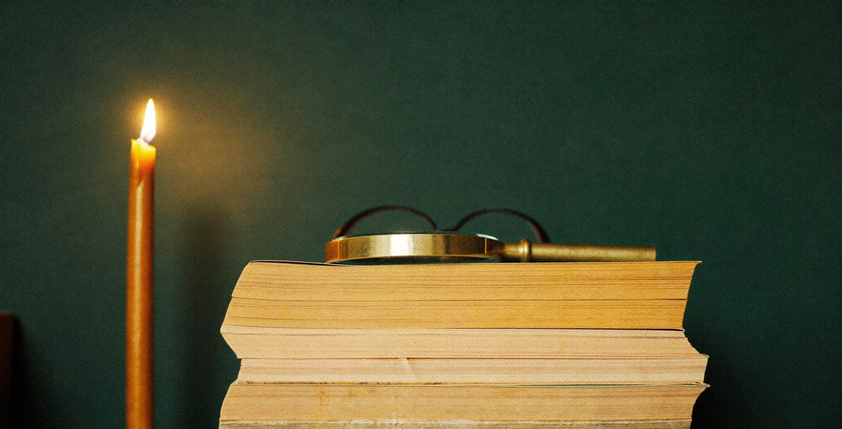 Stack of worn leather folios with a brass magnifying glass and reading spectacles beside a candle