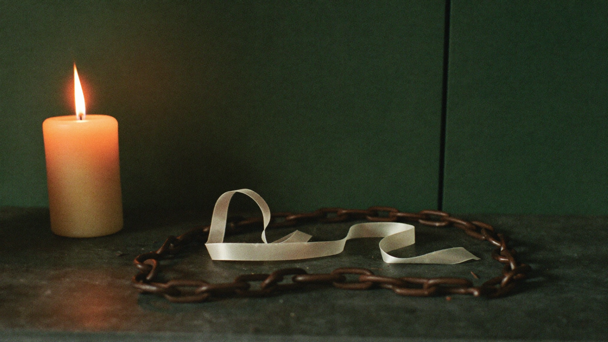 A pale silk ribbon lying coiled inside a heavy iron chain on dark stone, lit by a single candle