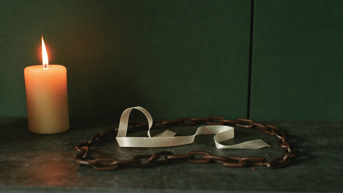 A pale silk ribbon lying coiled inside a heavy iron chain on dark stone, lit by a single candle