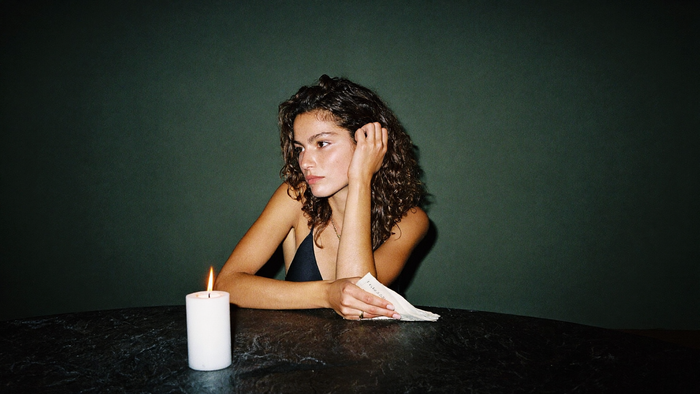 Woman at a dark stone table holding a folded paper note beside a burning white pillar candle
