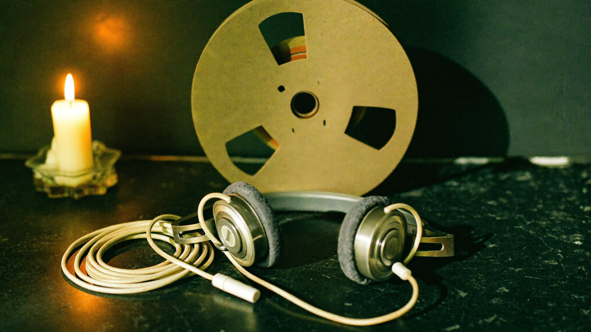 Vintage 1970s headphones and an open tape reel on dark stone, a single candle burning at the left