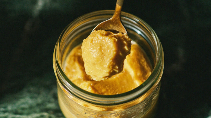 Golden cultured ghee lifted on a brass spoon from an open glass jar in warm candlelight