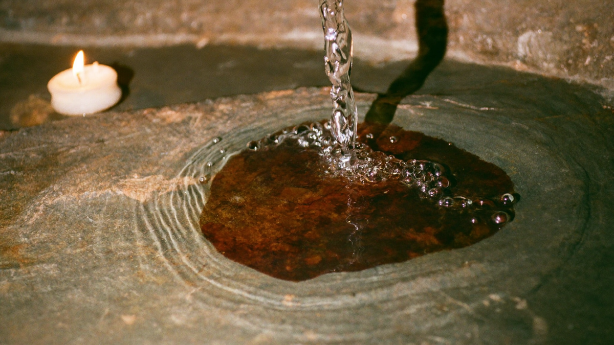 Clear water running over rust-red iron-stained stone into a shallow basin, lit by a single candle