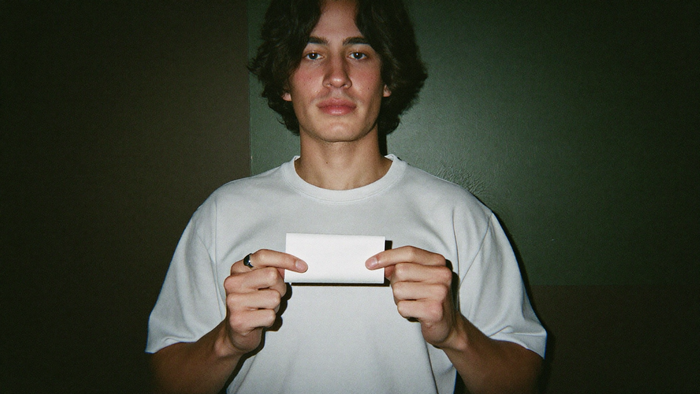 Young man holding a blank white paper slip in both hands against a dark green wall