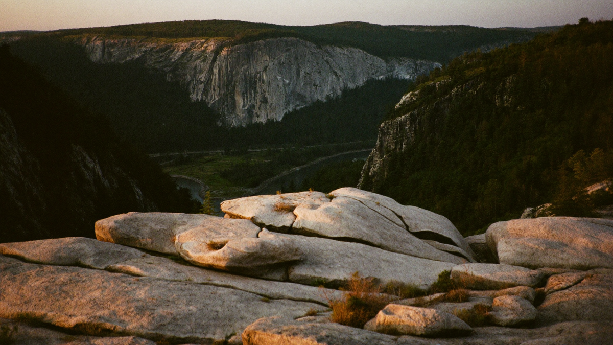 Pale granite rock plateau above a deep forested river gorge at dusk, a steep cliff rising opposite