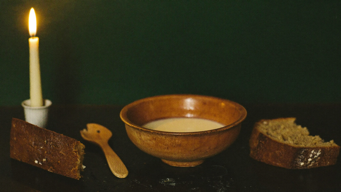 A bowl of milk, a wooden spoon, bread and a candle set out as a house-spirit offering
