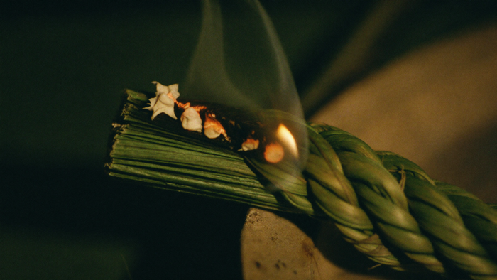 Smouldering cut end of a braided sweetgrass rope glowing orange with thin smoke rising in candlelight