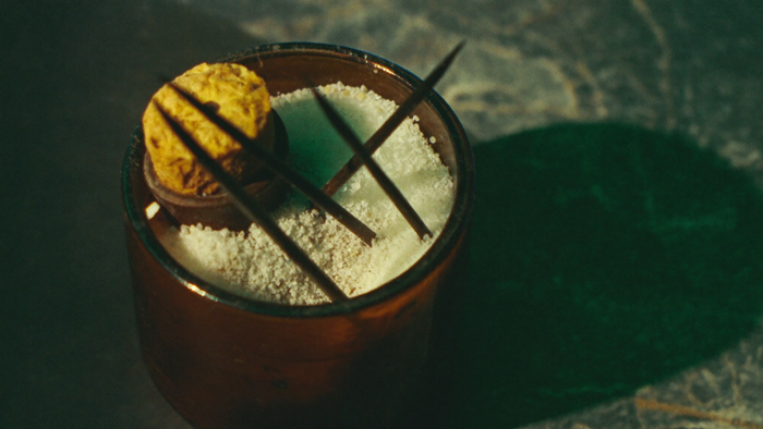 Coarse white salt and dark iron nails inside an open apothecary jar on dark green stone, cork resting on the rim