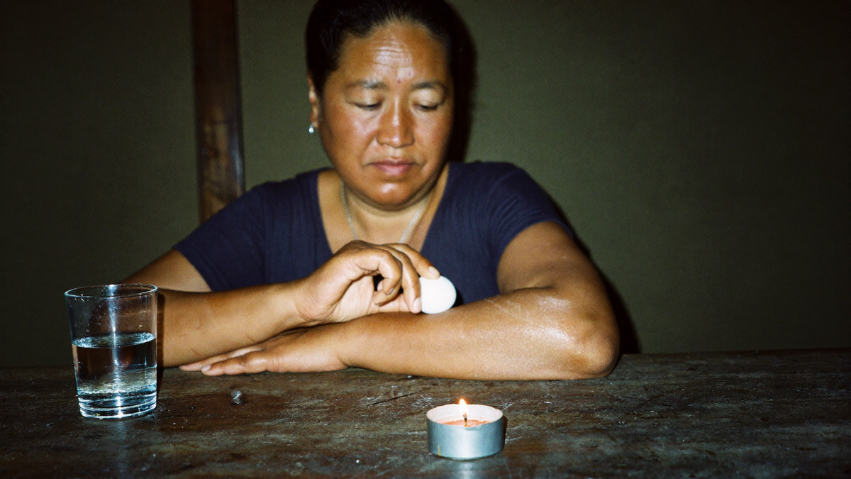 Woman passing a raw white egg along her forearm in an egg cleanse, a glass of water and a lit candle on the table
