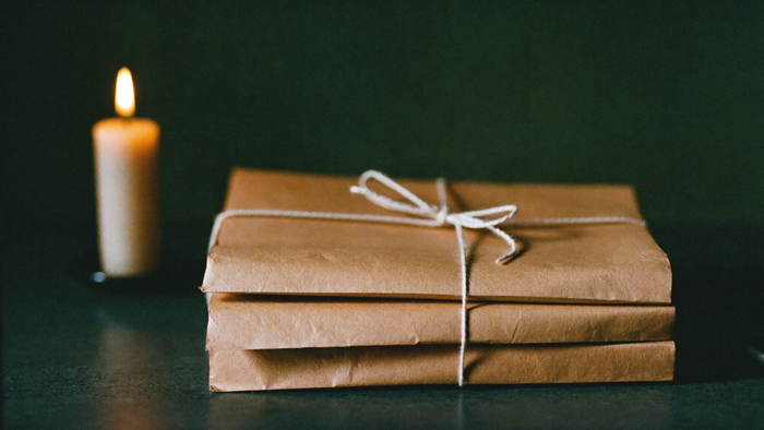 A stack of papers tied with twine on a dark stone table beside a burning candle
