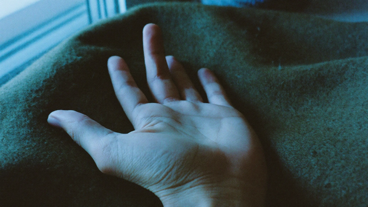 An open hand resting palm-up on a dark green wool blanket in cool early morning light from a window