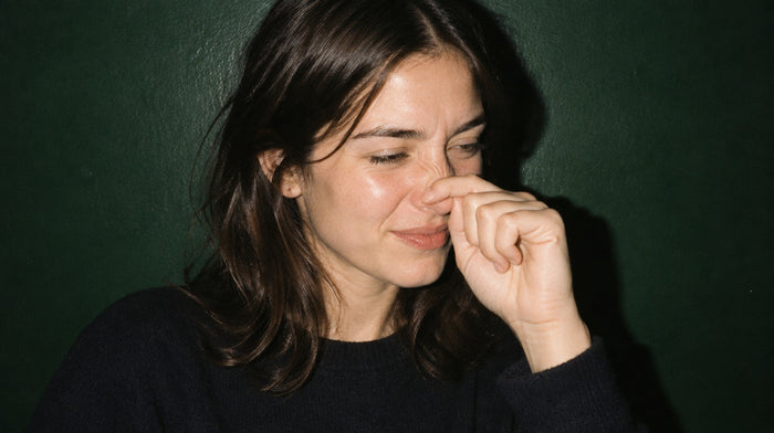 Young woman rubbing the tip of her itchy nose with a bent finger, smiling, against a dark green wall