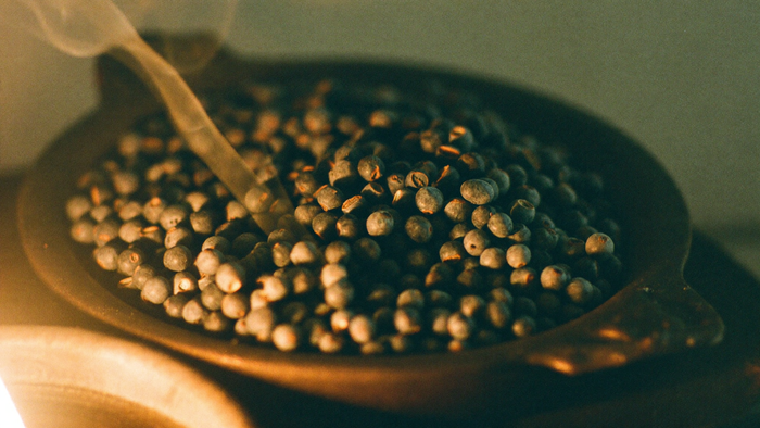 Dried blue-grey juniper berries heaped in a shallow iron dish with a thin thread of smoke rising