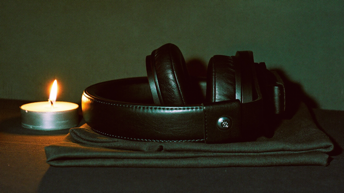 Over-ear headphones resting on folded dark linen beside a burning candle