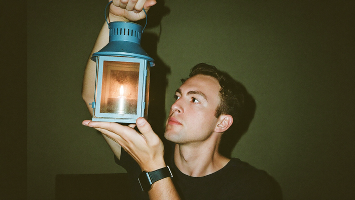 Young man holding up a lantern with a burning candle against a dark green wall