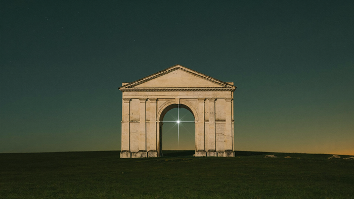 A lone stone gateway on a dark hillside at night with one bright star burning in the arch opening