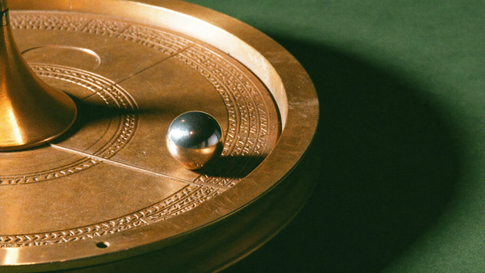 Brass astrolabe disc engraved with orbital rings, a small polished sphere resting on one track, against a dark green wall