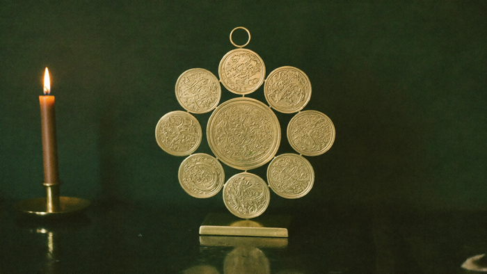 Brass ornament of interlocking circles standing on a dark altar surface, lit warmly by a single candle to the left