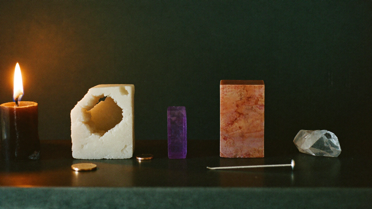 Minerals of increasing hardness in a row beside a copper coin and a steel nail, lit by one candle