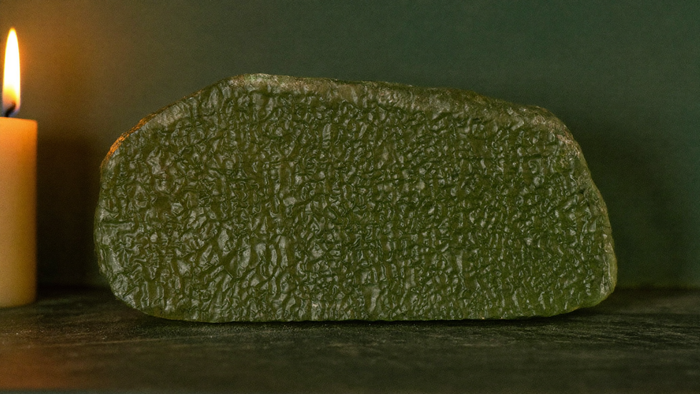 Raw green moldavite with a deeply furrowed surface beside a burning candle