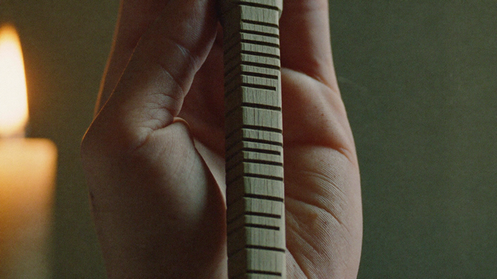A hand holding a wooden stave carved with ogham notches in candlelight