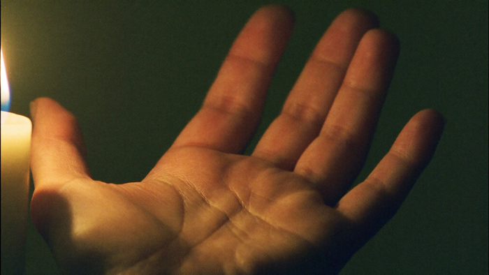 An open upturned palm lit warmly by candlelight with the creases of the hand clearly visible