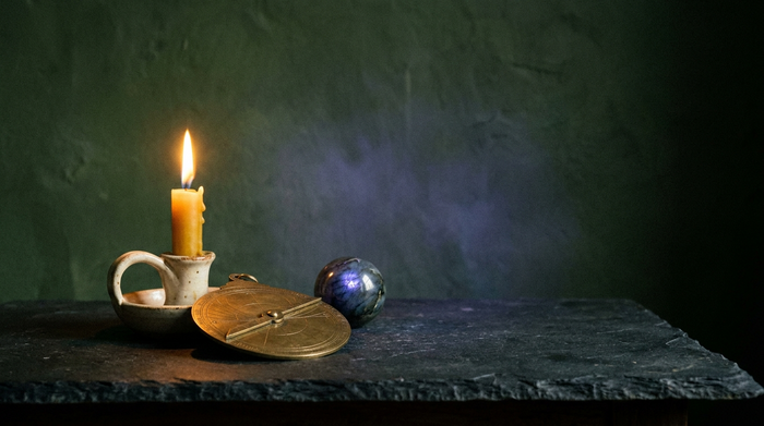 Burning beeswax candle, brass astrolabe and a labradorite sphere on a dark stone table