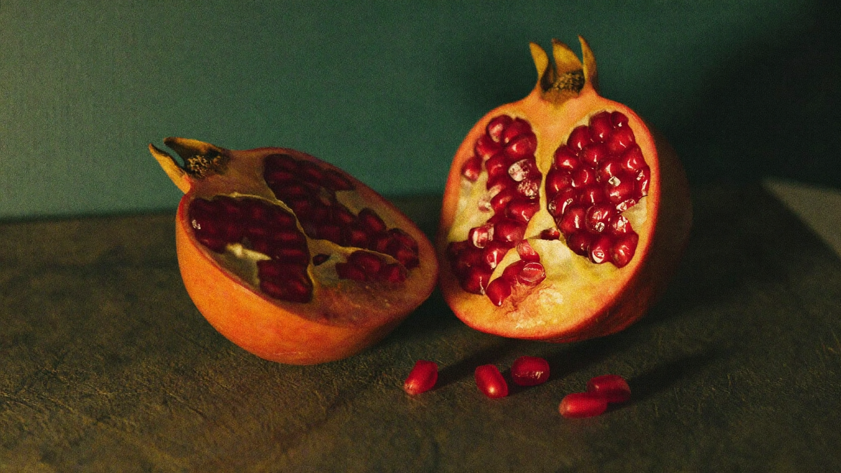 Pomegranates cut open on dark stone, garnet seeds in pale membrane, loose seeds beside them in candlelight