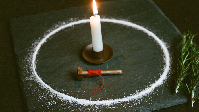 Closed circle of white salt on dark slate around a burning white candle, with an iron nail wrapped in red thread