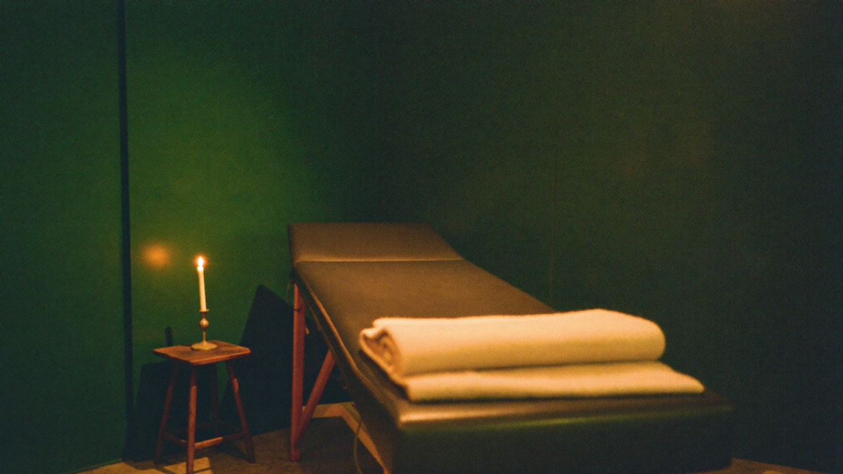 Empty padded treatment table with a folded blanket, lit by one candle in a dim green room