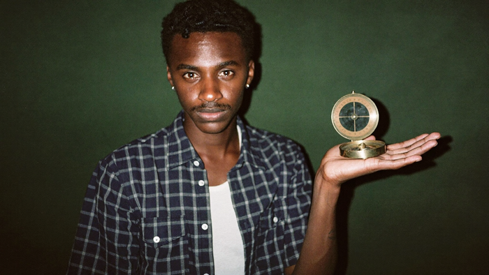 Young man holding a brass compass flat in his open palm against a dark green wall