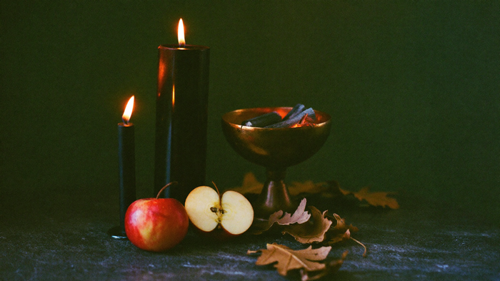 Black pillar candle, brass censer and a halved apple on a dark stone Samhain altar