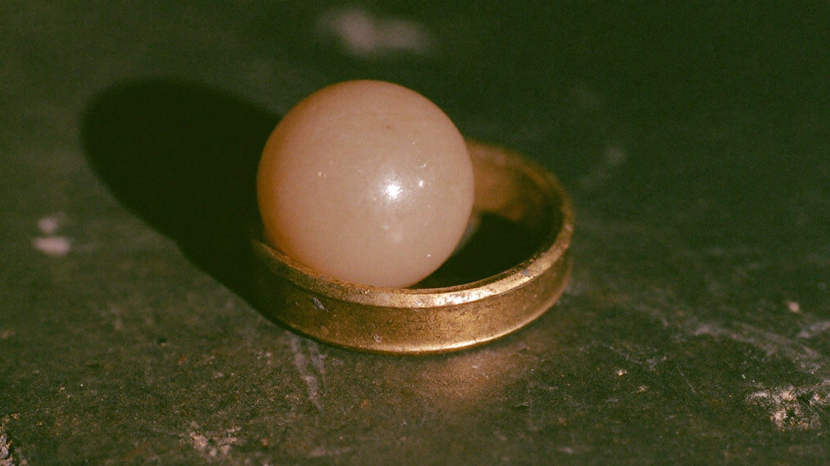 Pale stone sphere resting inside a tarnished brass ring on dark stone in warm light