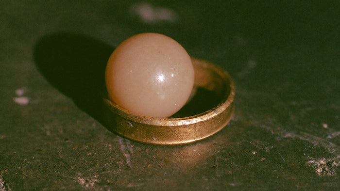 Pale stone sphere resting inside a tarnished brass ring on dark stone in warm light