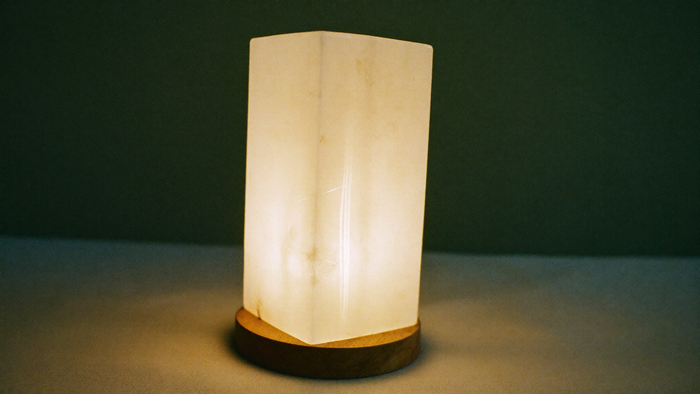 Glowing white selenite lamp on a turned wooden base against a dark green wall