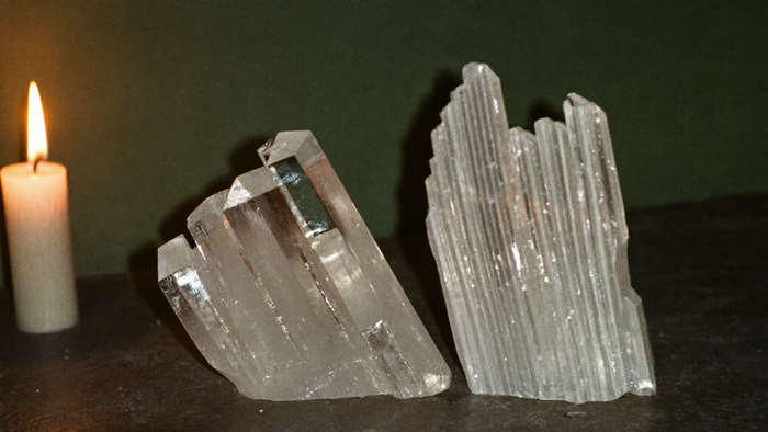 Glassy selenite blade beside a fibrous satin spar piece on dark stone in warm candlelight